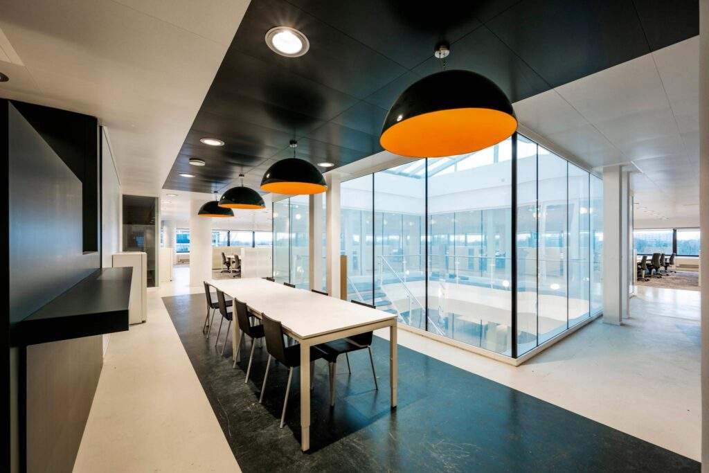 Moderne kantoorruimte aan de Prof. E.M. Meijerslaan met glazen wanden, vergadertafels en opvallende zwarte hanglampen met oranje binnenzijde.